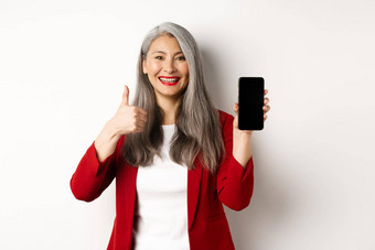 满意亚洲上了年纪的女商人显示空白智能手机屏幕翘拇指赞扬在线促销活动公司应用程序站白色背景