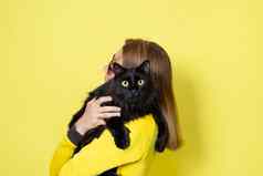 女孩黄色的衣服持有亲爱的毛茸茸的黑色的猫黄色的眼睛黄色的背景宠物护理概念