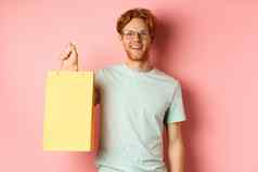 英俊的年轻的男人。购买礼物持有购物袋微笑相机站粉红色的背景