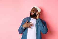 快乐非裔美国人男人。会说话的移动电话笑微笑站无檐小便帽牛仔布衬衫粉红色的背景