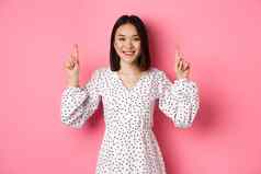 美丽的朝鲜文年轻的女人衣服显示公告指出手指促销复制空间微笑快乐站粉红色的背景