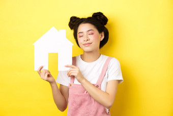 真正的房地产家庭概念梦幻微笑亚洲女人明亮的化妆显示纸房子断路关闭眼睛做白日梦购买财产黄色的背景