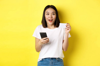 <strong>电子</strong>商务在线购物概念兴奋亚洲女人订单互联网持有智能<strong>手机</strong>塑料信贷卡站黄色的背景