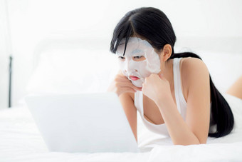 美丽的年轻的亚洲女人表面部面具说谎工作移动PC电脑床上卧室美女孩应用脸面具护肤品皱纹首页皮肤护理健康健康