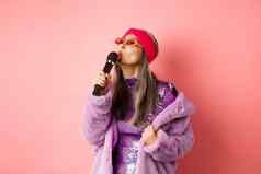 时尚的亚洲高级女人唱歌首歌执行卡拉ok麦克风站聚会，派对装人造皮毛外套粉红色的背景