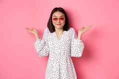 可爱的亚洲女人旅游微笑相机耸笨不要穿时尚的太阳镜白色衣服站粉红色的背景