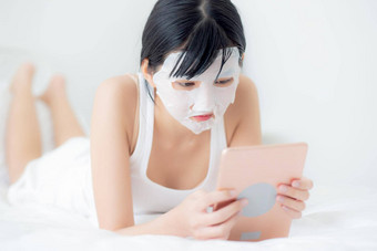 美丽的年轻的亚洲女人表面部面具说谎看平板电脑电脑床上卧室美女孩应用脸面具<strong>护肤品</strong>皱纹首页皮肤护理健康健康