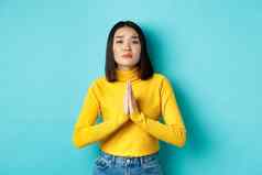 年轻的有吸引力的亚洲女孩乞讨支持持有手祈祷站蓝色的背景