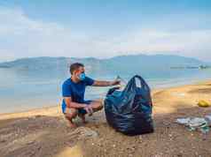 男人。手套选择塑料袋污染海问题泄漏垃圾垃圾垃圾海滩沙子引起的人为造成的污染运动清洁志愿者概念