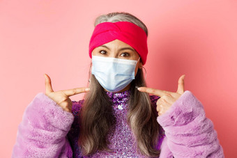 科维德病毒时尚概念时尚亚洲高级女人时尚的装指出手指医疗面具遵循社会距离规则粉红色的背景