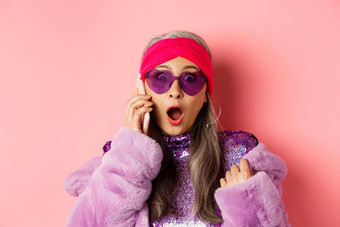 时尚特写镜头时尚的亚洲女人听到令人震惊的新闻智能手机喘气盯着惊讶相机穿时尚的太阳镜粉红色的背景