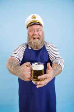 微笑肥胖男人。水手站光蓝色的背景焦点手啤酒