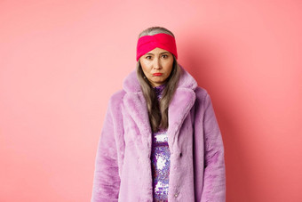 伤心悲观的时尚的亚洲高级女人心烦意乱相机生闷气的感觉陷入困境的站紫色的人造皮毛外套粉红色的背景