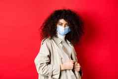 科维德流感大流行检疫概念时髦的女孩沟外套医疗面具把沟外套春天走红色的背景