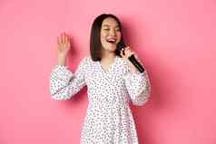 快乐亚洲女人唱歌麦克风有趣的卡拉ok酒吧站粉红色的背景