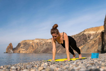 年轻的女人长头发健身教练黑色的运动服装紧身裤上衣伸展运动普拉提瑜伽席海阳光明媚的一天女健身瑜伽例程概念