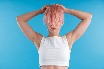 年轻的女人白色衬衫玩光滑的直粉红色的头发马尾辫隐藏脸摆姿势孤立的蓝色的工作室背景