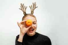 美丽的圣诞老人女孩驯鹿鹿角快乐金发女郎黑色的毛衣关闭橘子眼睛显示舌头