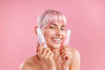 很高兴年轻的女人粉红色的头发持有塑料切除卵巢瓶美产品脸摆姿势孤立的粉红色的背景