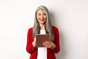 业务高级女企业家工作数字平板电脑微笑快乐相机穿红色的夹克化妆站白色背景