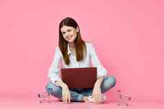 女人移动PC坐着地板上技术互联网购物粉红色的背景