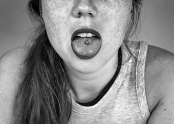 关闭肖像年轻的女人坚持穿舌头显示舌头穿刺黑色的白色