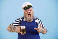 兴奋有胡子的男人。超重水手西装点啤酒光蓝色的背景