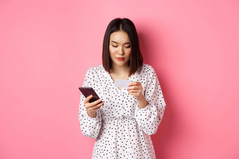 美丽的亚洲女人输入信贷卡信息移动电话应用程序购物<strong>在线支付</strong>订单智能手机站粉红色的背景