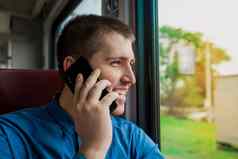 年轻的欧洲浅黑肤色的女人的家伙蓝色的衬衫笑着说微笑窗口会说话的移动电话现代电火车