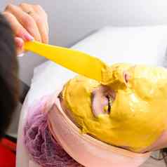 水疗中心治疗美沙龙手专业美容师应用黄金面具客户的脸