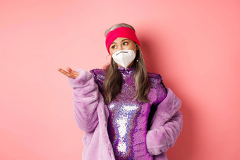 科维德流感大流行时尚概念时尚的亚洲高级女人呼吸器聚会，派对衣服持怀疑态度指出手左站粉红色的背景