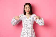 可爱的亚洲女人衣服指出手指复制空间显示产品折扣微笑站粉红色的背景