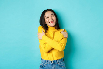 快乐的美丽的女孩拥抱身体微笑拥抱站无忧无虑的黄色的套衫蓝色的背景