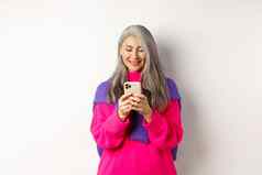 美丽的亚洲高级女人粉红色的时尚的毛衣智能手机夫人阅读移动电话微笑站白色背景