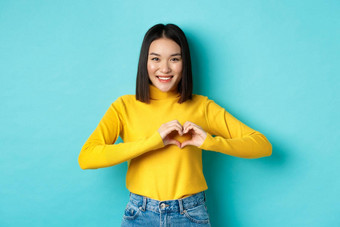 情人节一天浪漫概念美丽的亚洲女人显示爱心手势微笑站蓝色的背景