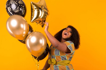 假期聚会，派对有趣的概念肖像微笑年轻的非裔美国人年轻的女人甜蜜的黄色的背景持有气球