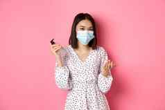 科维德流感大流行生活方式概念可爱的亚洲女人清洁手洗手液防腐剂穿脸面具站粉红色的背景