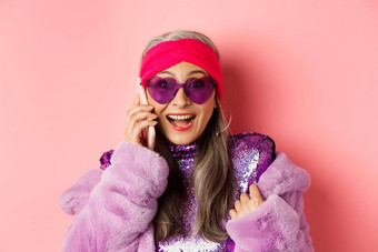 时尚特写镜头时尚的亚洲高级女人听到令人惊异的新闻移动电话微笑快乐相机穿时尚的太阳镜粉红色的背景