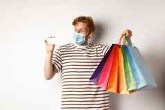 流感大流行特殊的提供概念快乐红色头发的人男人。脸面具显示购物袋塑料信贷卡站白色背景