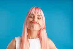 肖像好玩的年轻的女人自然长粉红色的染色头发持有海滩头发胡子摆姿势孤立的蓝色的工作室背景