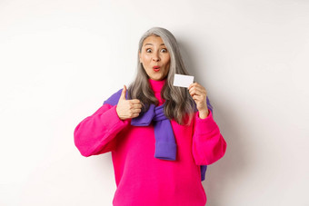 购物概念微笑亚洲中年女人灰色头发显示塑料信贷卡竖起大拇指<strong>推荐</strong>银行促销活动白色背景