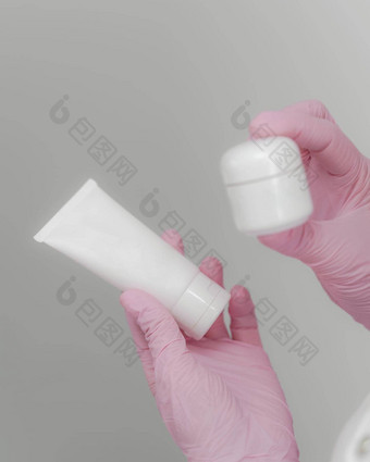 女手粉红色的手套持有瓶奶油容器身体乳液化妆品管专业护理产品皮肤护理广告概念布局风格复制空间孤立的灰色的