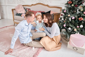 爱的家庭妈妈爸爸拥抱女儿父母婴儿孩子有趣的圣诞节树白色壁炉在室内快乐圣诞节快乐一年快乐的漂亮的人