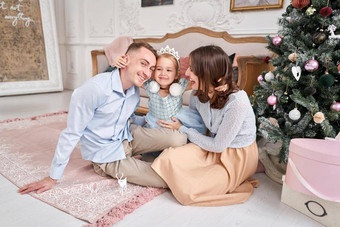 爱的家庭妈妈爸爸拥抱女儿<strong>父母</strong>婴儿孩子有趣的圣诞<strong>节</strong>树白色壁炉在室内快乐圣诞<strong>节</strong>快乐一年快乐的漂亮的人