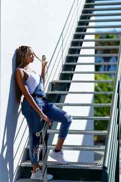 年轻的黑色的女人非洲式发型辫子城市楼梯携带滑板
