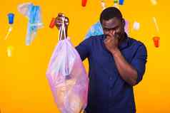 环境污染塑料回收问题浪费处理概念愤怒的非洲美国男人。持有垃圾袋黄色的背景感觉气味垃圾
