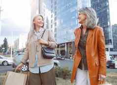 快乐成熟的女士们购物袋走现代城市街