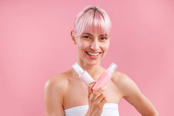 兴奋年轻的女人粉红色的头发微笑显示<strong>塑料切</strong>除卵巢瓶美产品摆姿势孤立的粉红色的背景