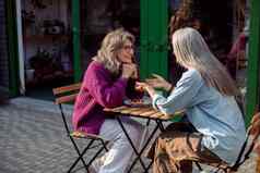 银头发的女人告诉故事成熟的朋友坐着表格在户外