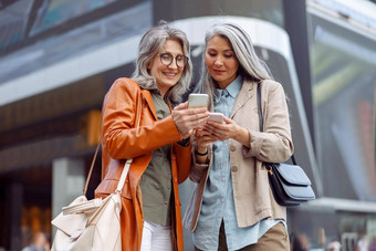 积极的灰色头发的女士们移动手机现代城市街